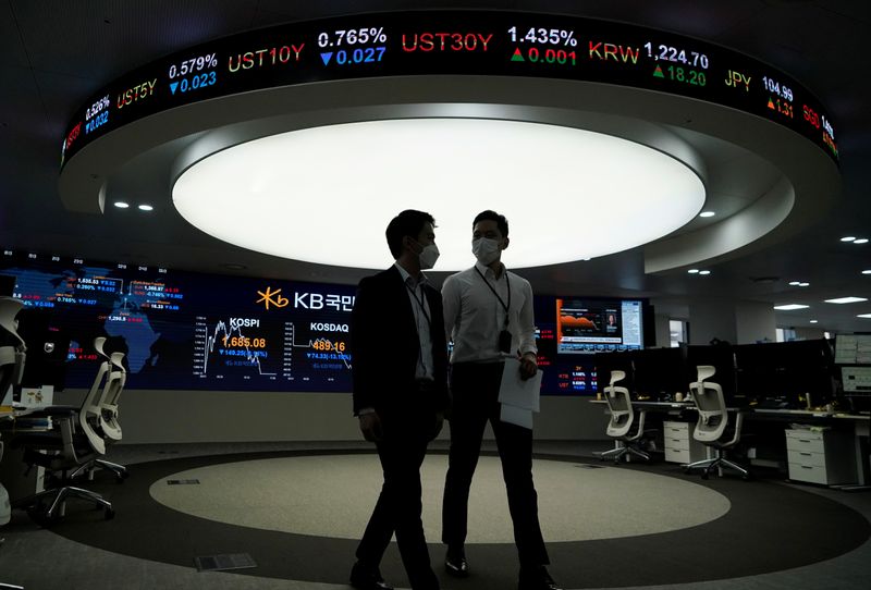 © Reuters. Currency dealers walk past an electronic board showing the Korea Composite Stock Price Index (KOSPI) at a dealing room of a bank in Seoul