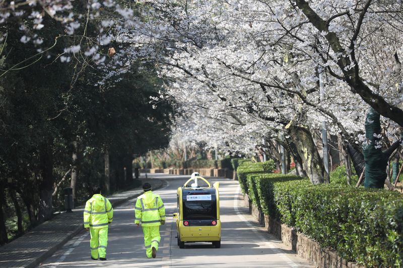 © Reuters. Security personnel walk next to a 5G enabled autonomous vehicle, installed with a camera filming blooming cherry blossoms for an online live-streaming session, inside the closed Wuhan University