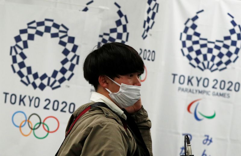 © Reuters. A man wearing a protective face mask, following an outbreak of the coronavirus disease (COVID-19), walks in front of flags of the Tokyo 2020 Olympic and Paralympic Games in Tokyo