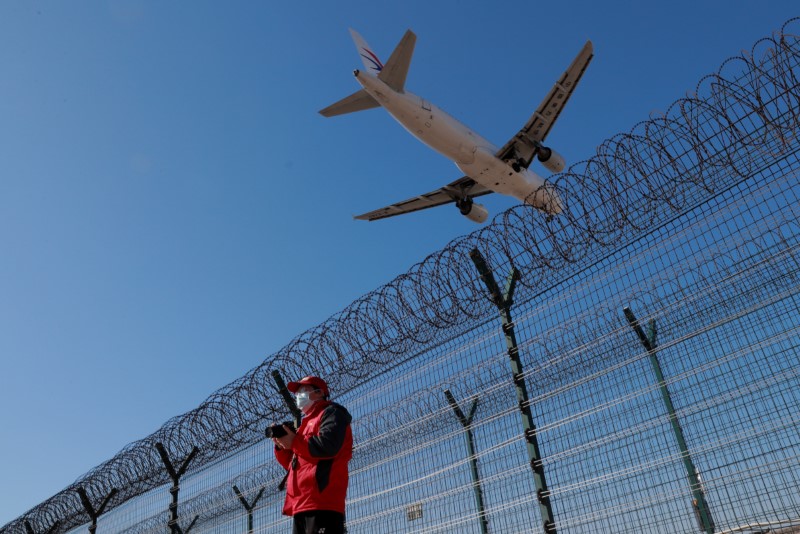 © Reuters. A man wearing a protective mask stands at a fence surrounding Beijing Capital International as a plane lands in Beijing as the country is hit by an outbreak of the novel coronavirus