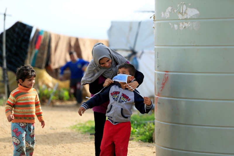 © Reuters. A Syrian refugee woman puts a face mask on a boy as a precaution against the spread of coronavirus, in al-Wazzani area in southern Lebanon