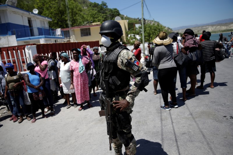 © Reuters. A Haitian National Police officer looks on as Haitians stand behind him in the in the border of Malpasse