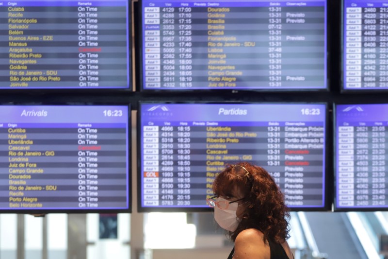 © Reuters. FILE PHOTO: Woman wearing a face mask stands in front of arrival and departure electronic boards after the Brazilian airline Azul stated that it will cut all of its international flights out of its main hub due to the coronavirus outbreak