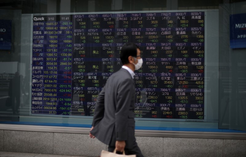 © Reuters. A man wearing protective face mask walks in front of a stock quotation board outside a brokerage in Tokyo