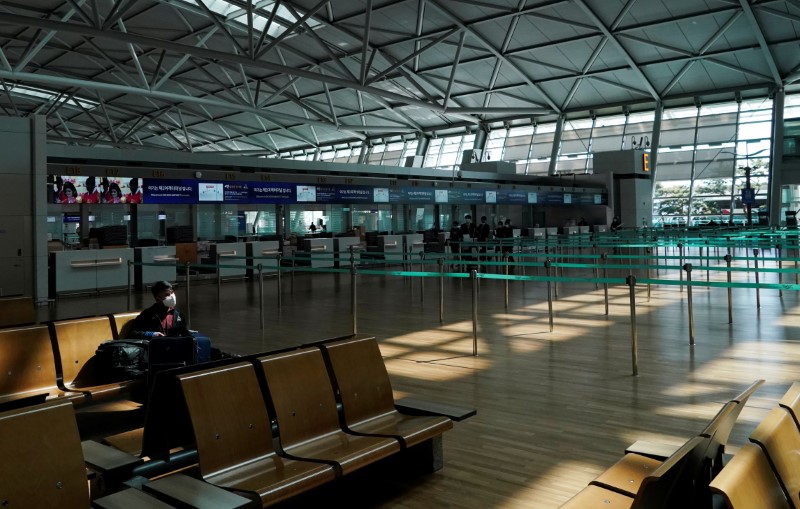 © Reuters. A man wearing a mask to prevent contracting the coronavirus waits for his flight next to an empty check in booth at Incheon International Airport in Incheon