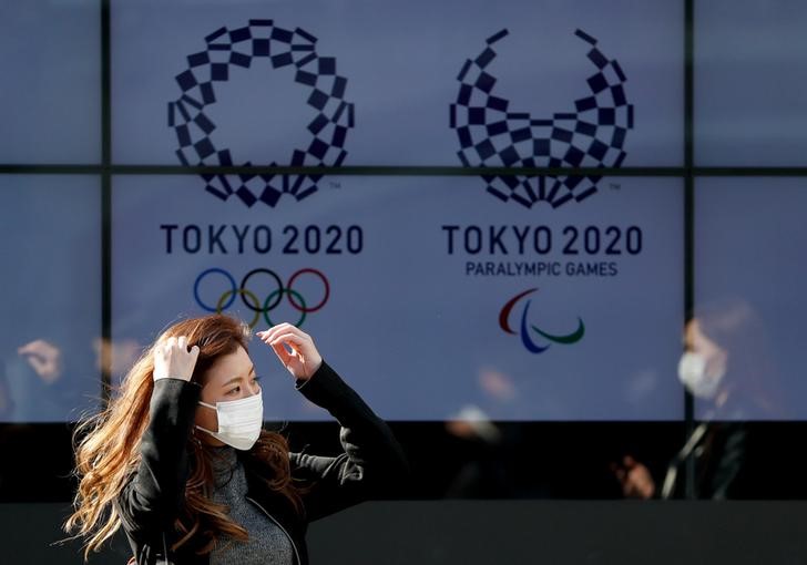 &copy; Reuters. A passerby wearing a protective face mask following an outbreak of the coronavirus disease (COVID-19) walks past a screen displaying logos of Tokyo 2020 Olympic and Paralympic Games in Tokyo