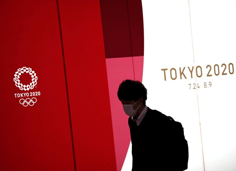&copy; Reuters. Homem usando máscara de proteção passa em frente a painel com logo da Olimp;iada Tóquio 2020 em Tóquio