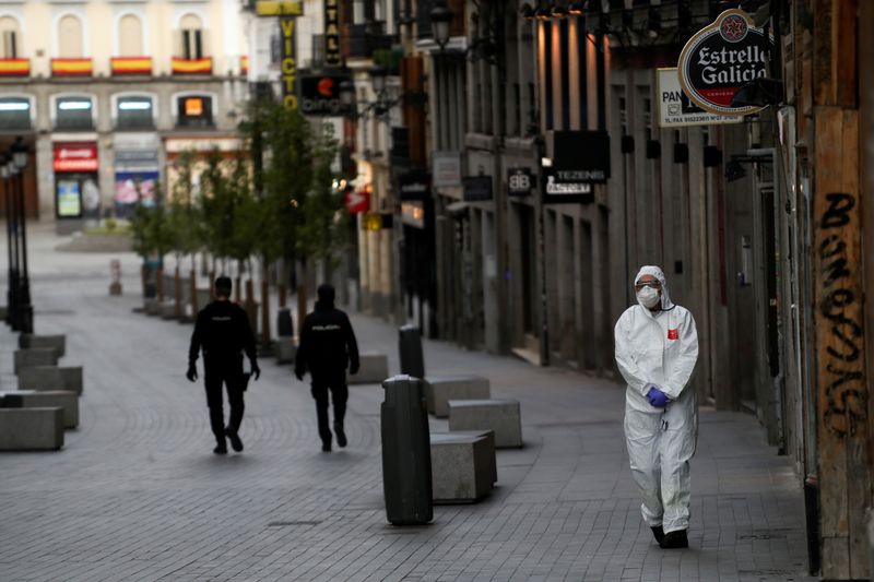 &copy; Reuters. FOTO DE ARCHIVO: Un trabajador sanitario en traje protector camina cerca de dos agentes de policía que patrullan una calle desierta durante el brote de coronavirus en Madrid