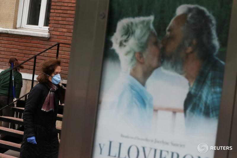 &copy; Reuters. Una mujer con mascarilla pasa junto a un cartel publicitario por una calle de Madrid, España.