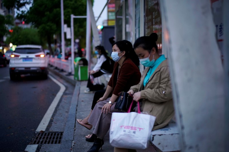 &copy; Reuters. Women wearing face masks wait for buses at a bus stop in Xianning