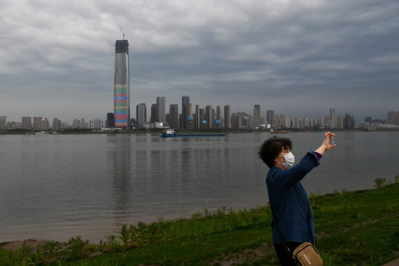 &copy; Reuters. Woman wearing a face mask takes pictures with a mobile phone at a riverside park in Wuhan