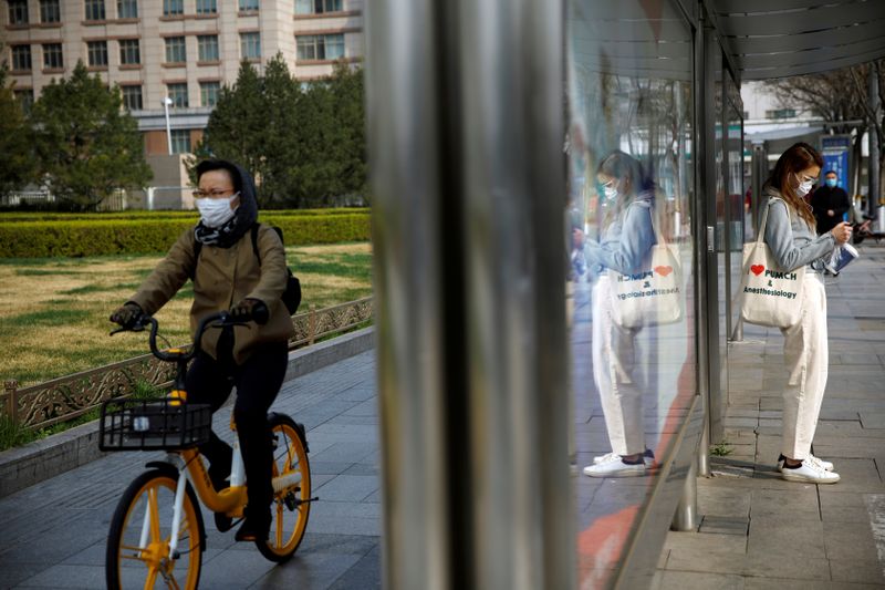 &copy; Reuters. Gente usando mascarillas cerca de una parada de autobús en una calle después del brote de coronavirus (COVID-19), en Pekín