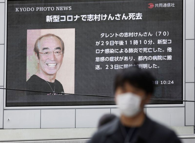 &copy; Reuters. Un hombre con mascarilla camina frente a pantalla que muestra reporte sobre la muerte del comediante Ken Shimura, Osaka