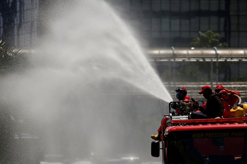 &copy; Reuters. Firefighters spray disinfectant using high pressure pump truck to prevent the spread of coronavirus disease (COVID-19), on the main road in Jakarta