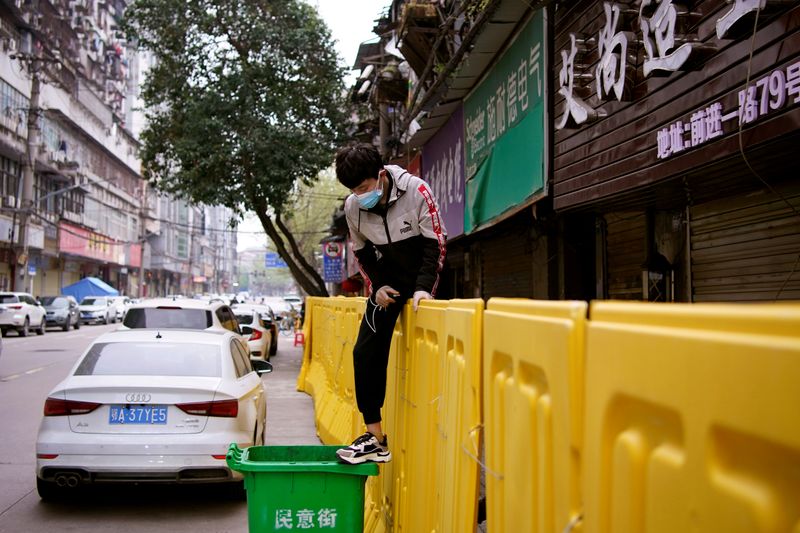 &copy; Reuters. Jovem de máscara pula barreira de isolamento construída para separar prédios de rua em Wuhan