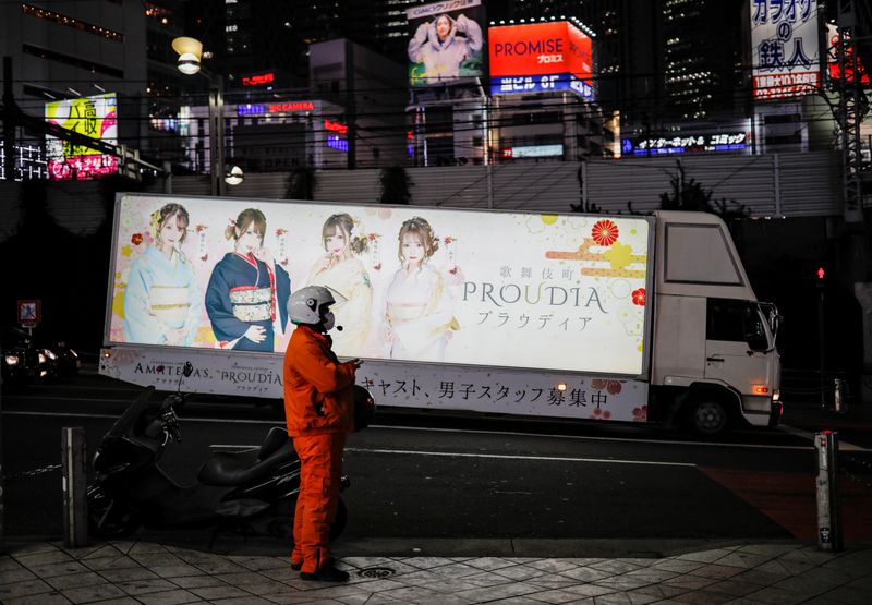 &copy; Reuters. A biker wearing a protective face mask, following the outbreak of the coronavirus disease, stands on the street as a truck with advertisements of a night club runs past at Shinjuku district in Tokyo