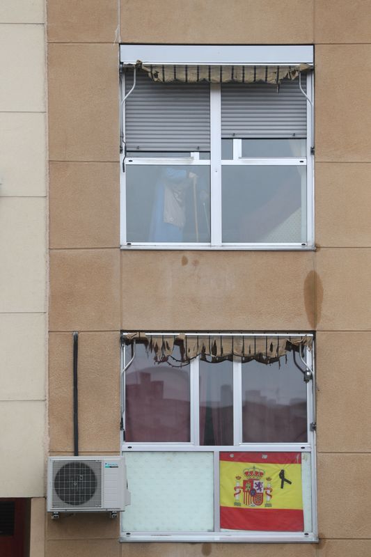 &copy; Reuters. FOTO DE ARCHIVO: Una bandera española y una cinta negra de luto se exhiben en un edificio mientras una anciana es vista a través de su ventana durante el brote de la enfermedad coronavirus (COVID-19) en Madrid, España