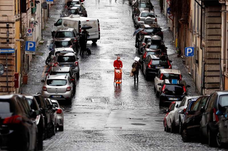 &copy; Reuters. FOTO DE ARCHIVO: Un hombre con una mascarilla protectora empuja un carrito de compras por una calle casi vacía durante el brote de coronavirus en Roma