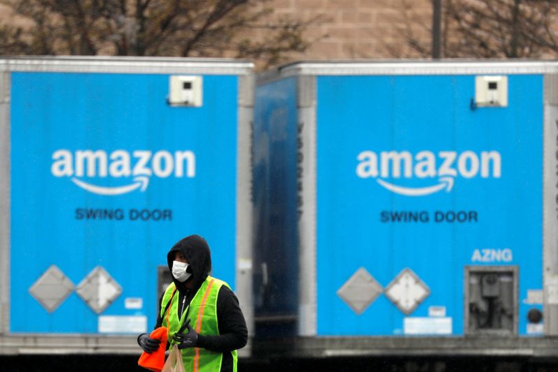 © Reuters. FILE PHOTO: A worker in a face mask walks by trucks parked at an Amazon facility as the global coronavirus outbreak continued in Bethpage on Long Island in New York