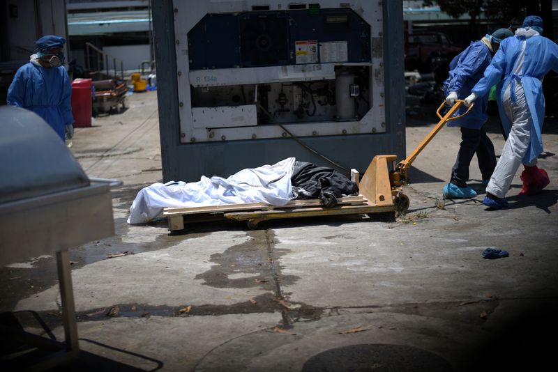 &copy; Reuters. Health workers wearing protective gear bring a dead body past a refrigerated container outside of Teodoro Maldonado Carbo Hospital amid the spread of the coronavirus disease (COVID-19), in Guayaquil