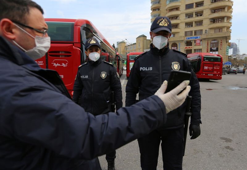 © Reuters. Мужчина показывает сотрудникам правоохранительных органов разрешение на выход из дома после введения ограничений в связи с распространением коронавируса в Баку