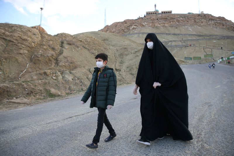 &copy; Reuters. Com máscara e luvas de proteção contra novo coronavírus, mulher e seu filho caminham por estrada do Irã