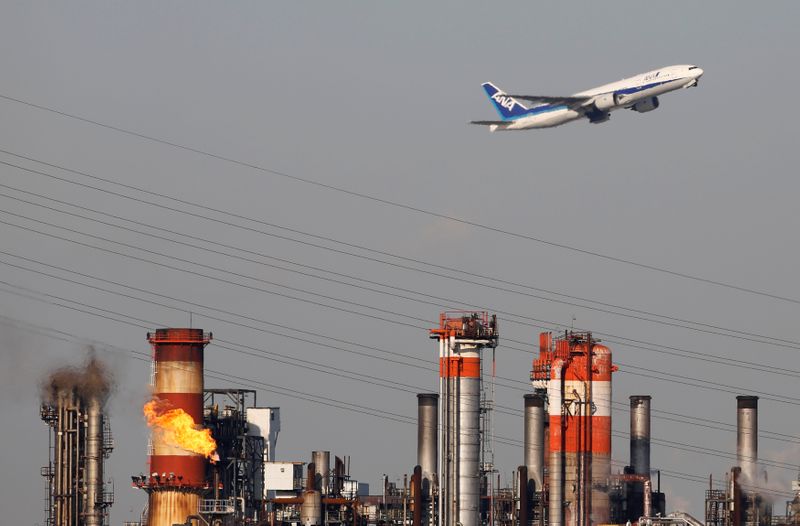 © Reuters. FILE PHOTO: An All Nippon Airways' plane flies over a chimney of an oil refinery in Kawasaki