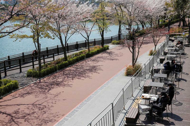 &copy; Reuters. People enjoy the view while practicing social distancing during the global spread of the coronavirus disease (COVID-19), at a cafe near a cherry blossom trees street  Seokchon Lake park, in Seoul