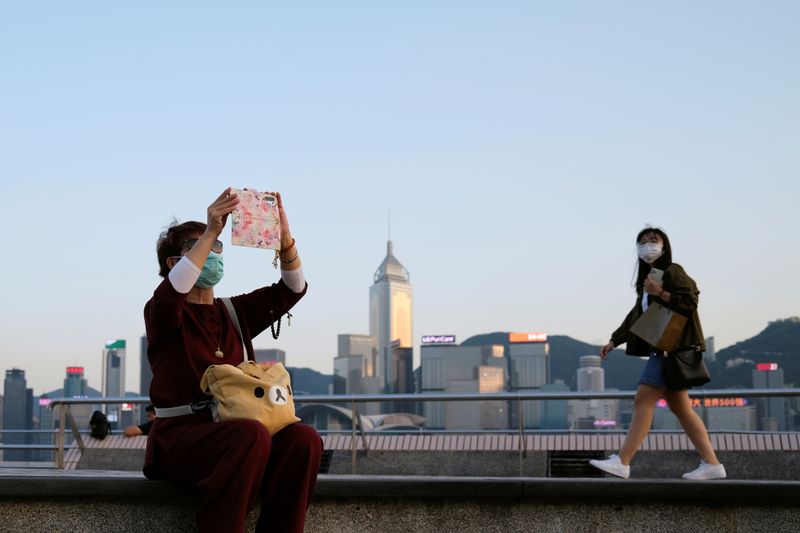 &copy; Reuters. FILE PHOTO: People with protective masks walk in front of Hong Kong&apos;s skyline