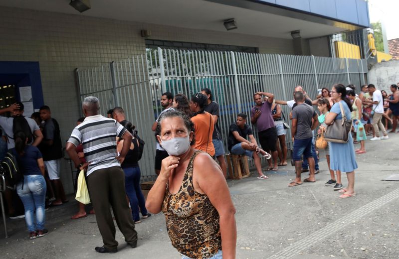 &copy; Reuters. Mulher usa máscara enquanto outras pessoas aguardam em fila de banco no Rio de Janeiro