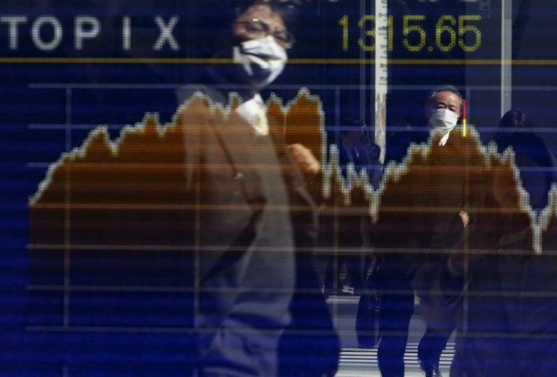 &copy; Reuters. Pedestrians wearing masks are reflected in an electronic board showing the graph of the recent fluctuations of the TOPIX outside a brokerage in Tokyo, Japan