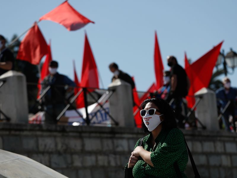 &copy; Reuters. Un miembro de la plataforma de coordinación del movimiento sindical griego, PAME, lleva una mascarilla protectora en la que se lee &quot;Las bocas tapadas tienen voz&quot; durante una manifestación en conmemoración del Primero del Trabajo, mientras con