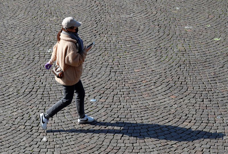 &copy; Reuters. A woman wearing a mask crosses an empty square in central Maastricht