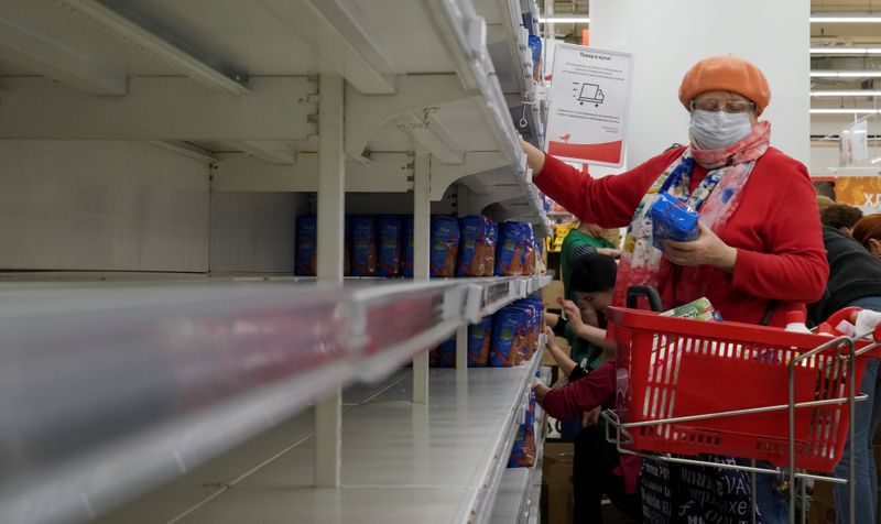 &copy; Reuters. FILE PHOTO: A woman, wearing a protective mask, holds a pack of buckwheat from a new delivery, next to empty shelves in a section for cereals and groats, in a supermarket in Moscow