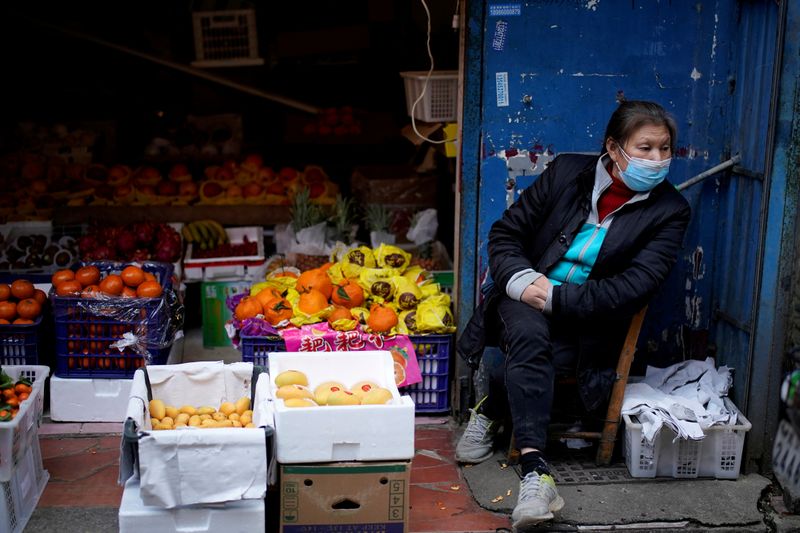 &copy; Reuters. FOTO DE ARCHIVO: Una mujer con mascarilla junto a un puesto de frutas en Wuhan