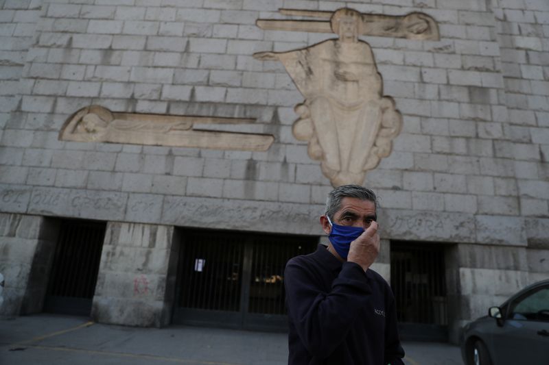 &copy; Reuters. Un trabajador ajusta su mascarilla mientras entrega información en la puerta cerrada de un cementerio en Santiago