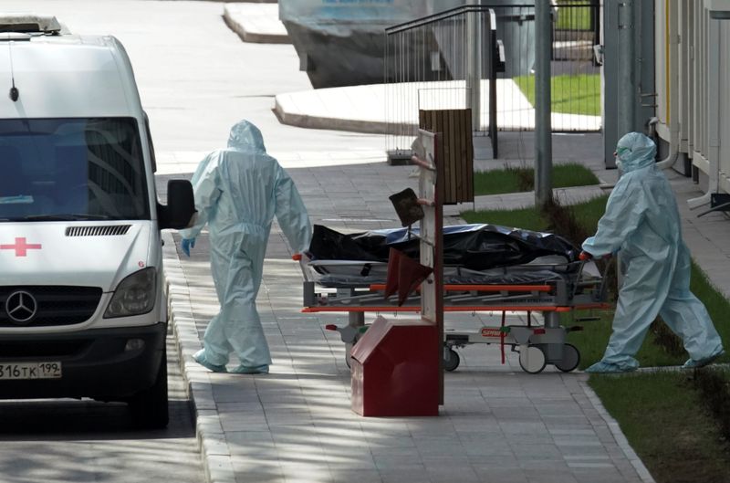 © Reuters. Медики в защитных костюмах везут каталку к машине скорой помощи возле подмосковной больницы, где лечат пациентов с коронавирусом