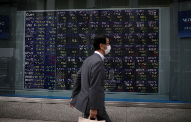 &copy; Reuters. Un uomo con una mascherina passa davanti a uno schermo con informazioni sugli indici delle Borse a Tokyo