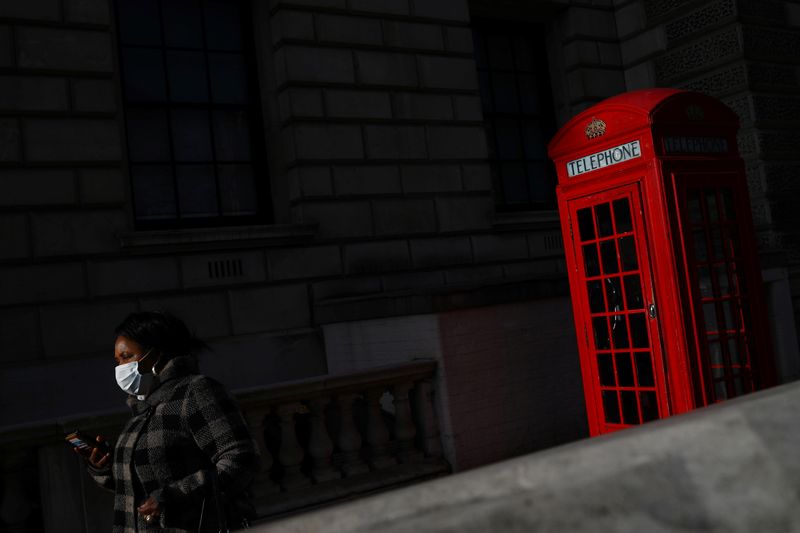 &copy; Reuters. Una mujer con una mascarilla pasa junto a una cabina telefónica en Westminster