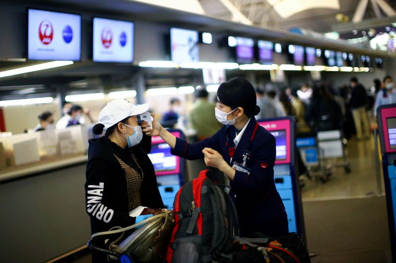 &copy; Reuters. FILE PHOTO: An employee of Japan Airlines (JAL), wearing protective mask following an outbreak of the coronavirus disease (COVID-19), scans the temperature to a passenger at the almost empty Kansai International Airport in Osaka