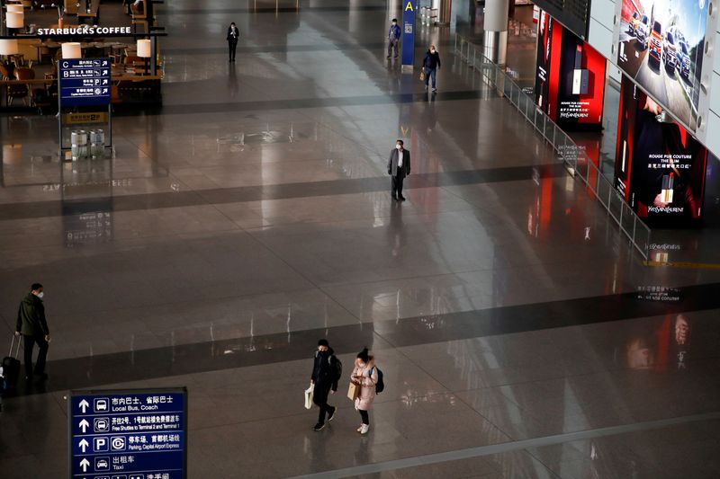 © Reuters. FILE PHOTO: March 16, 2020 picture of people wearing face masks walk at Beijing Capital International Airport