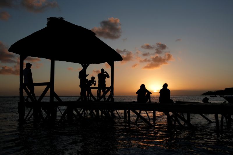 &copy; Reuters. FILE PHOTO: People look at the sunset from the beach in Bel Ombre