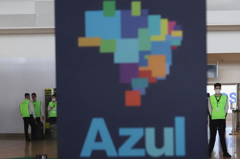 &copy; Reuters. Workers wearing face masks are seen next to a banner of Brazilian airline Azul, after the airline stated that it will cut all of its international flights out of its main hub due to the coronavirus outbreak, at Viracopos International Airport, in Campinas