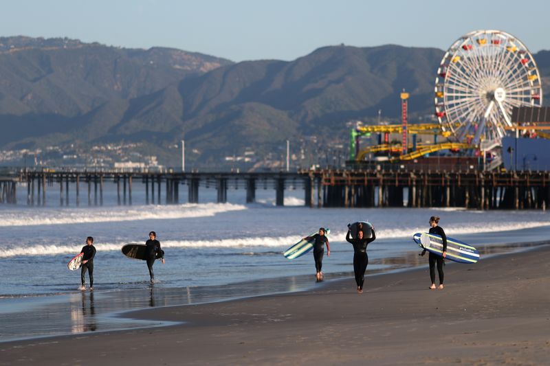 © Reuters. Los surfistas caminan por la playa el primer día de la apertura de las playas del condado de Los Ángeles en Santa Mónica