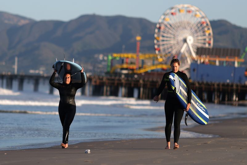 © Reuters. Surfers walk on the beach on the first day of the opening of LA County beaches in Santa Monica