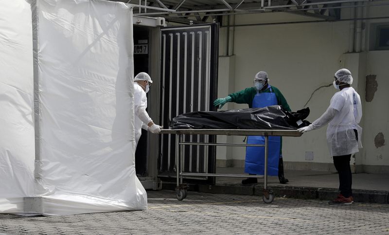 &copy; Reuters. Profissionais de saúde com trajes de proteção transportam cadáver para caminhão frigorífico durante pandemia de Covid-19 no Rio de Janeiro