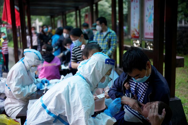 &copy; Reuters. Un trabajador médico con un traje de protección realiza una prueba de ácido nucleico a un niño en un complejo residencial en Wuhan, China.