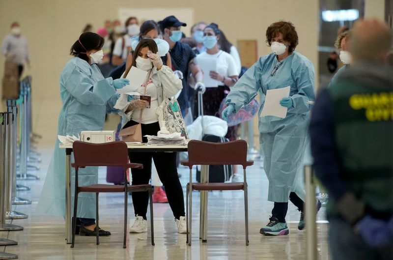 © Reuters. Pasajeros haciendo cola junto a santiarios vestidos con trajes de protección en el aeropuerto Adolfo Suárez Barajas, en Madrid, España