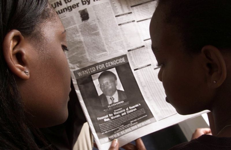 © Reuters. FILE PHOTO: READERS LOOK AT A PICTURE OF A RWANDAN WANTED FOR ALLEGED ROLE IN  RWANDA'S 1994 GENOCIDE.