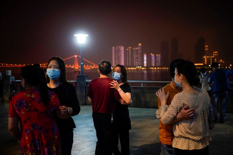 © Reuters. People wearing protective face masks dance under the Yangtze River Bridge in Wuhan